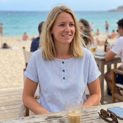 Vrouw draagt de Elodie Gestreepte Blouse op een strandterras